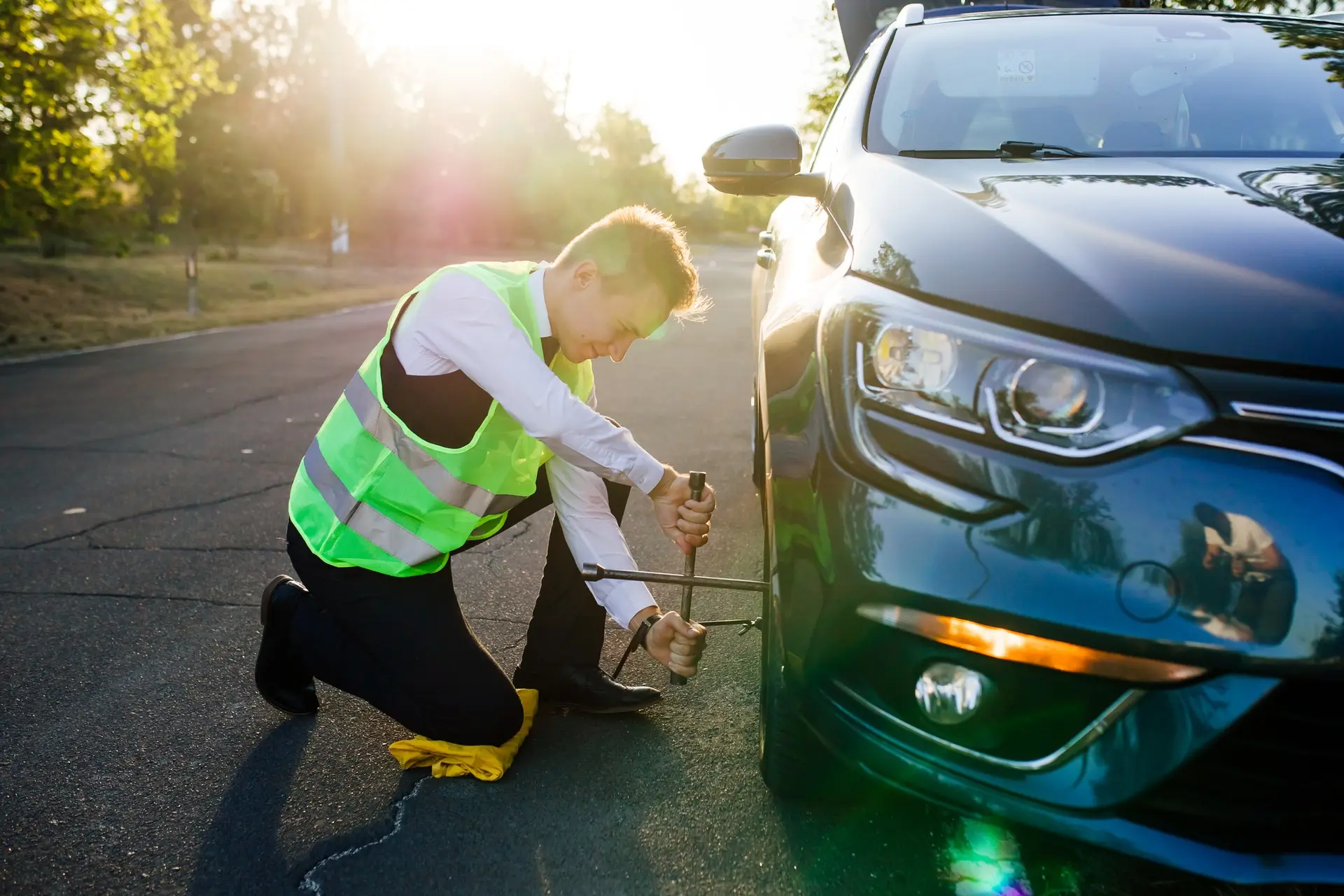 When Do You Need Emergency Tire Service? A man in a green safety vest changes a flat tire on a road.