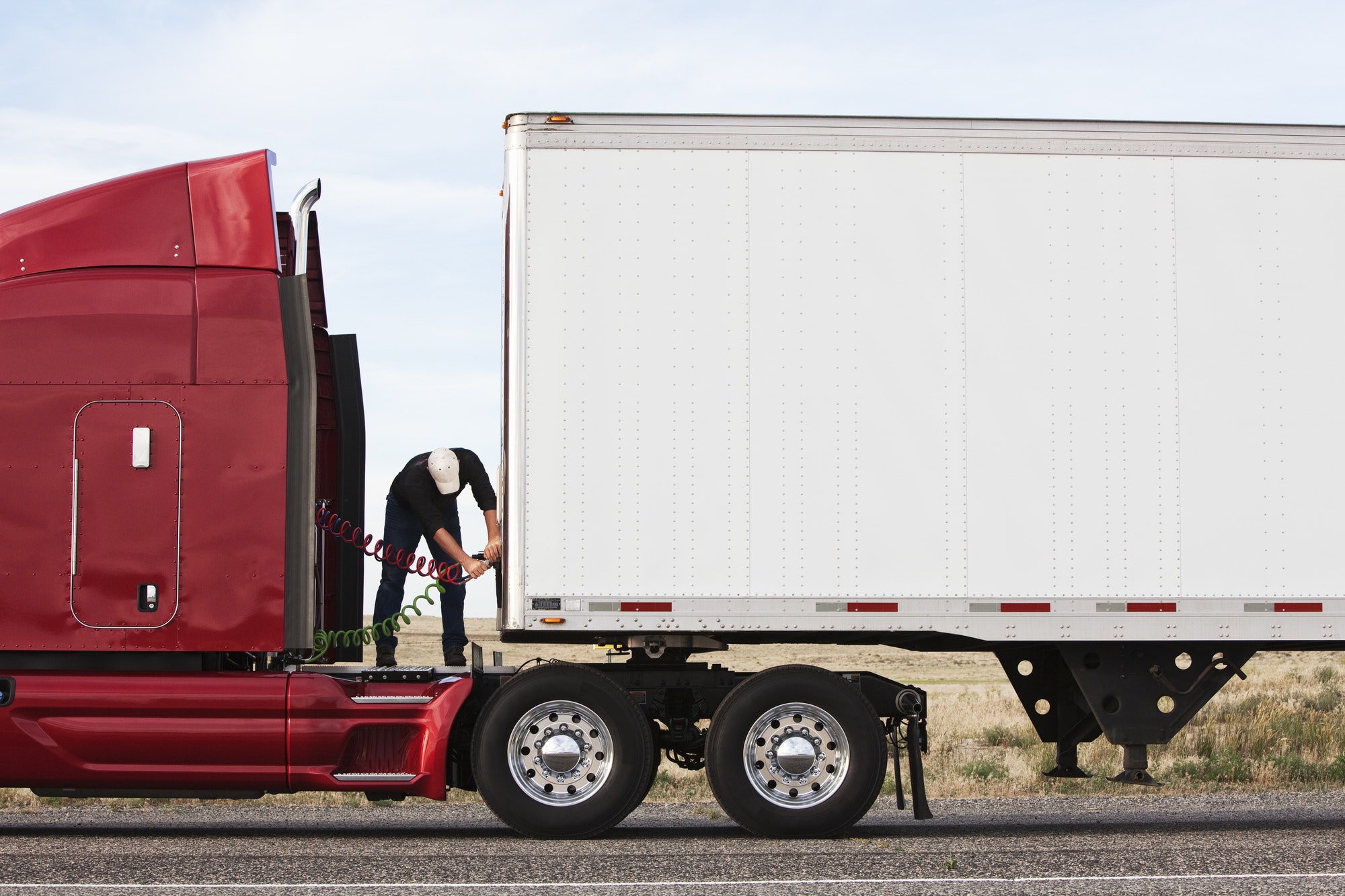 Why You Should Start Searching for Commercial Truck Roadside Assistance Near Me View of a driver connectiing the power cables to trailer of a commercial truck.